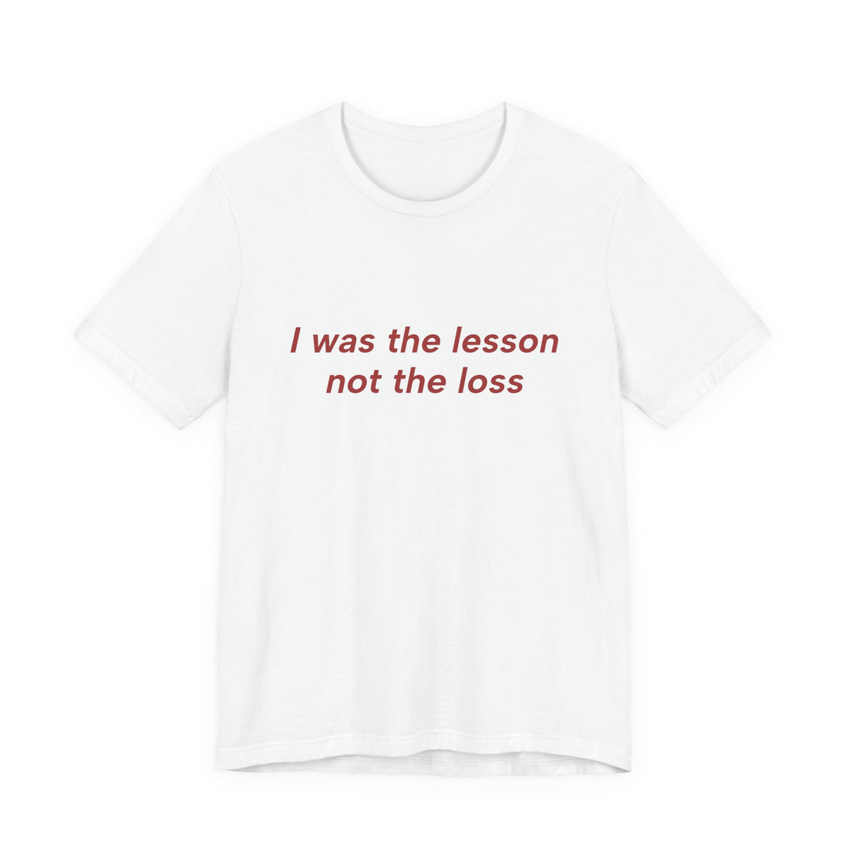 A white short-sleeve crewneck t-shirt with the phrase 'I was the lesson not the loss' printed in red serif text across the chest, displayed on a clean white background.