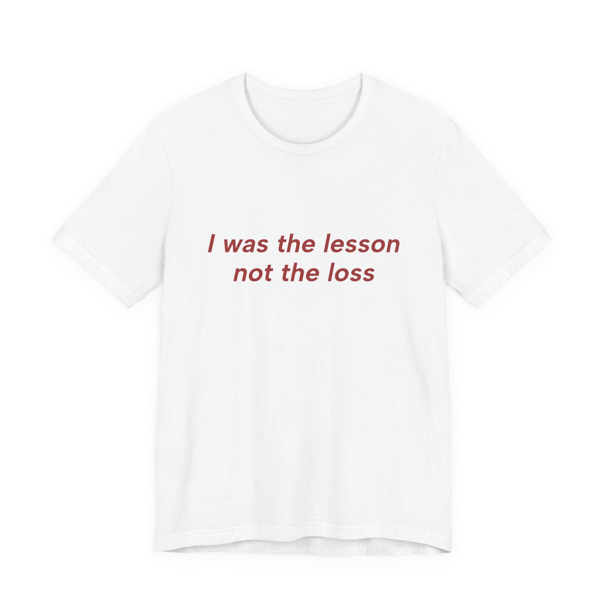 A white short-sleeve crewneck t-shirt with the phrase 'I was the lesson not the loss' printed in red serif text across the chest, displayed on a clean white background.