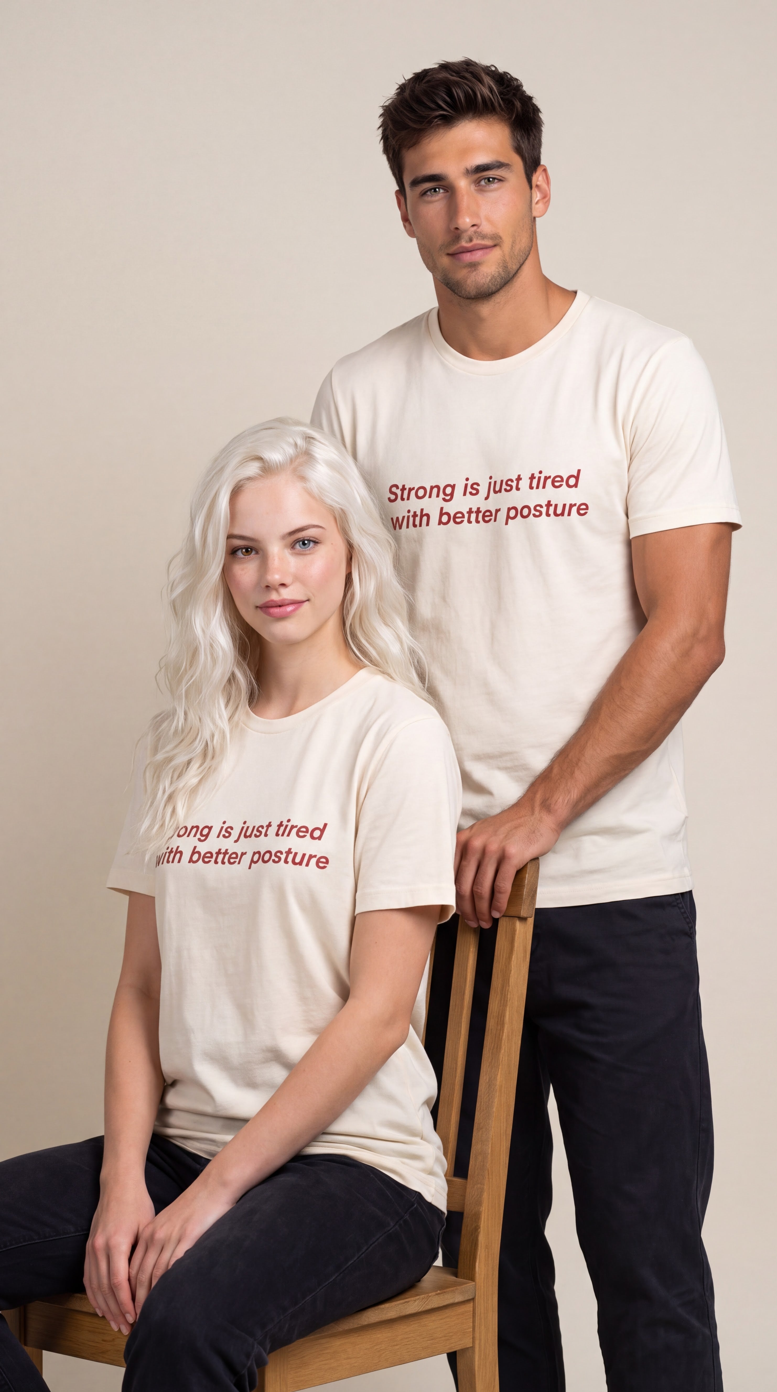 Two models wearing matching cream-colored graphic t-shirts with red text that reads 'Strong is just tired with better posture' and 'Strong is just tired with better posture' respectively, posed against a neutral beige background.