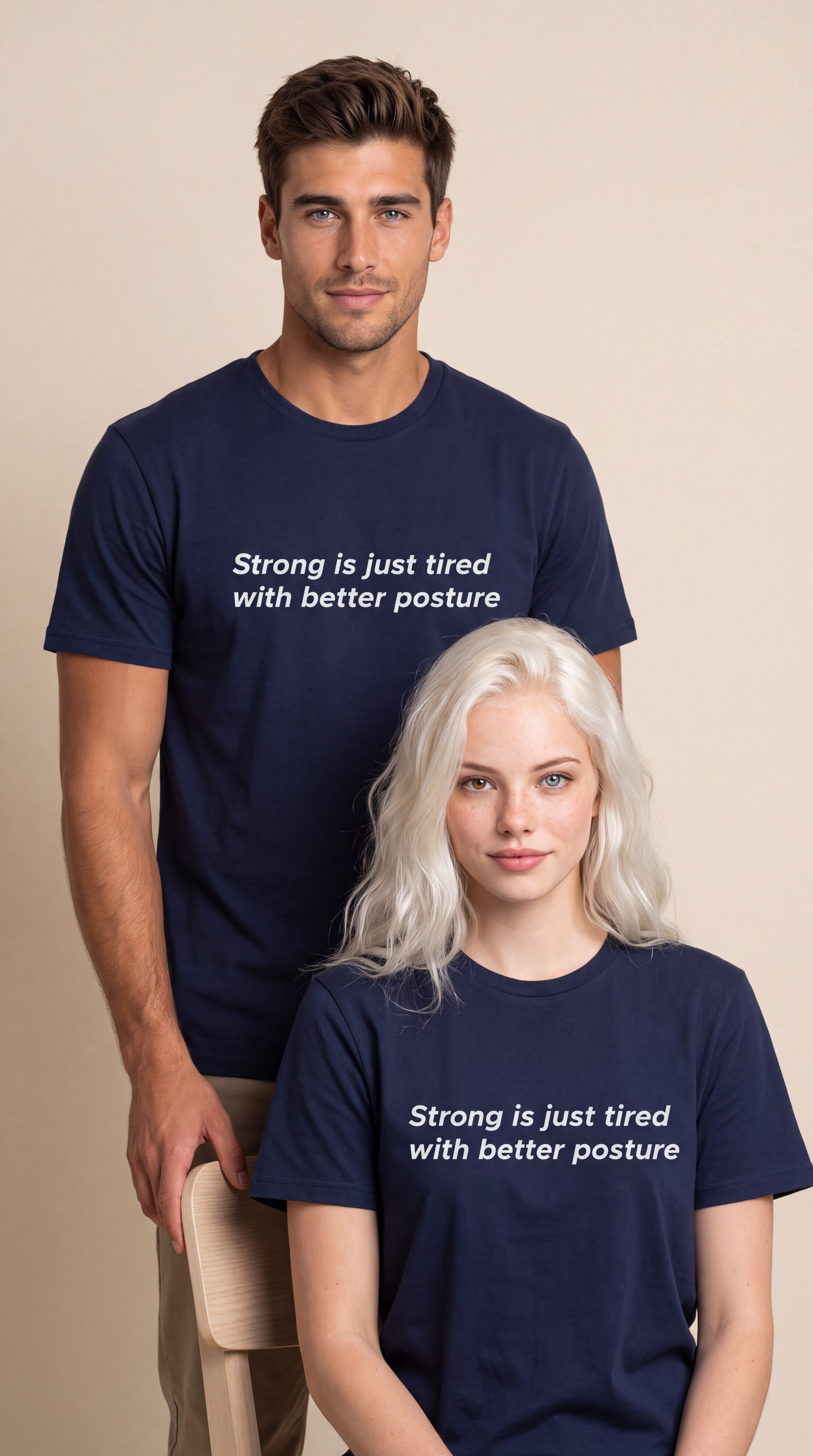 A man and a woman modeling matching navy blue t-shirts with the white printed text 'Strong is just tired with better posture' against a warm beige studio background.