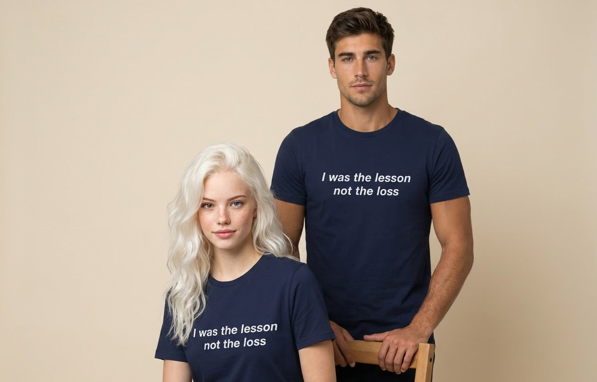 A man and a woman wearing matching navy blue t-shirts with the white printed text 'I was the lesson not the loss', posed against a solid beige background.