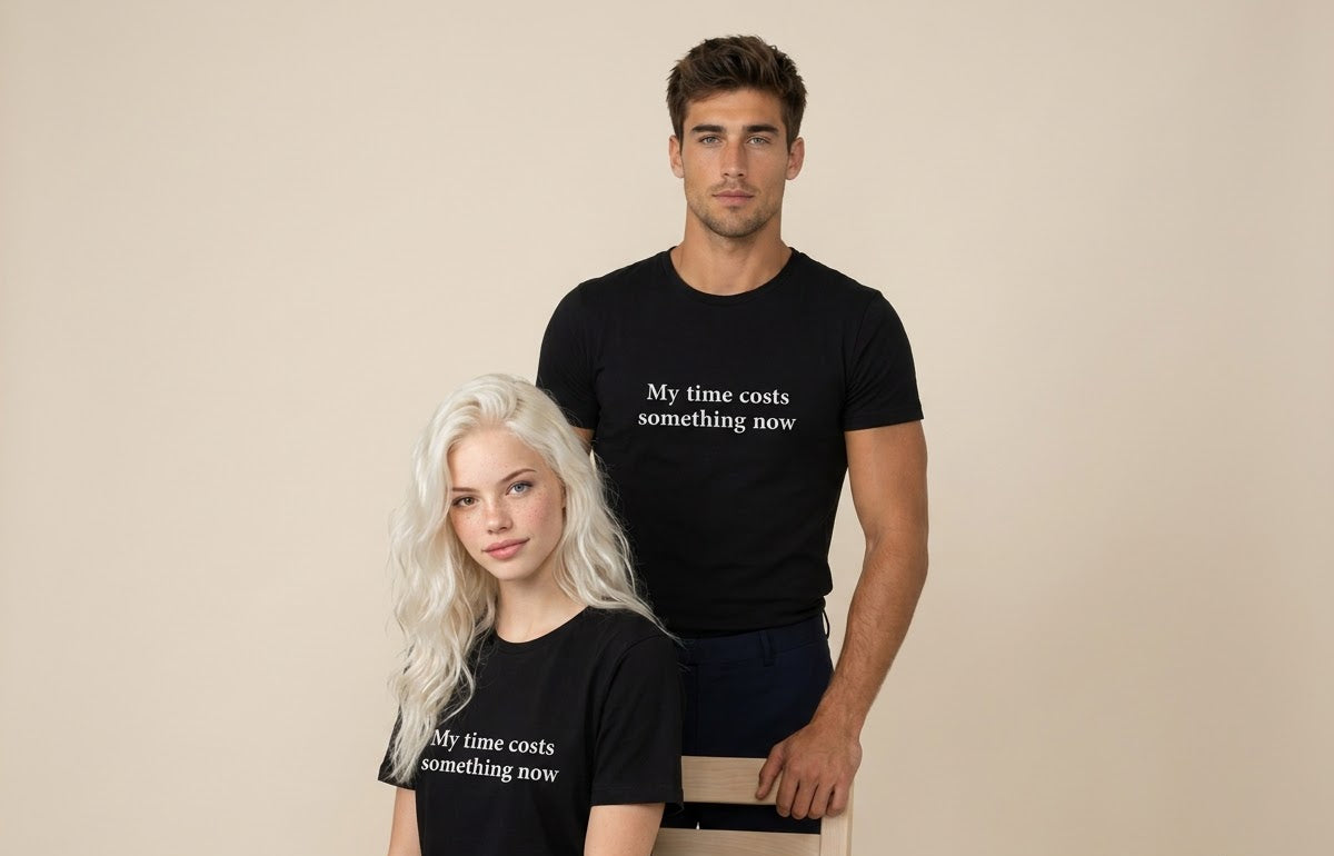 A man and a woman modeling matching black graphic t-shirts with the white printed text 'My time costs something now' against a solid beige studio background.