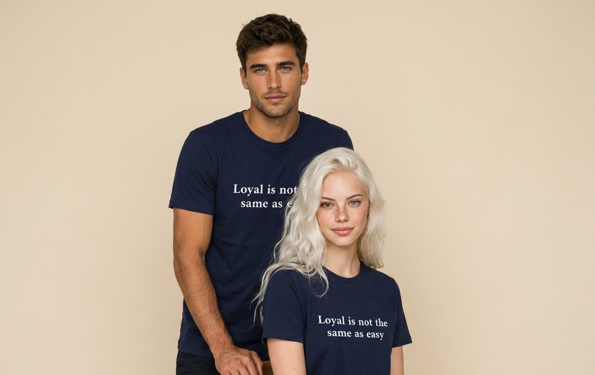 A man and a woman wearing matching navy blue t-shirts with the white printed text 'Loyal is not the same as easy', posed against a solid beige studio background.